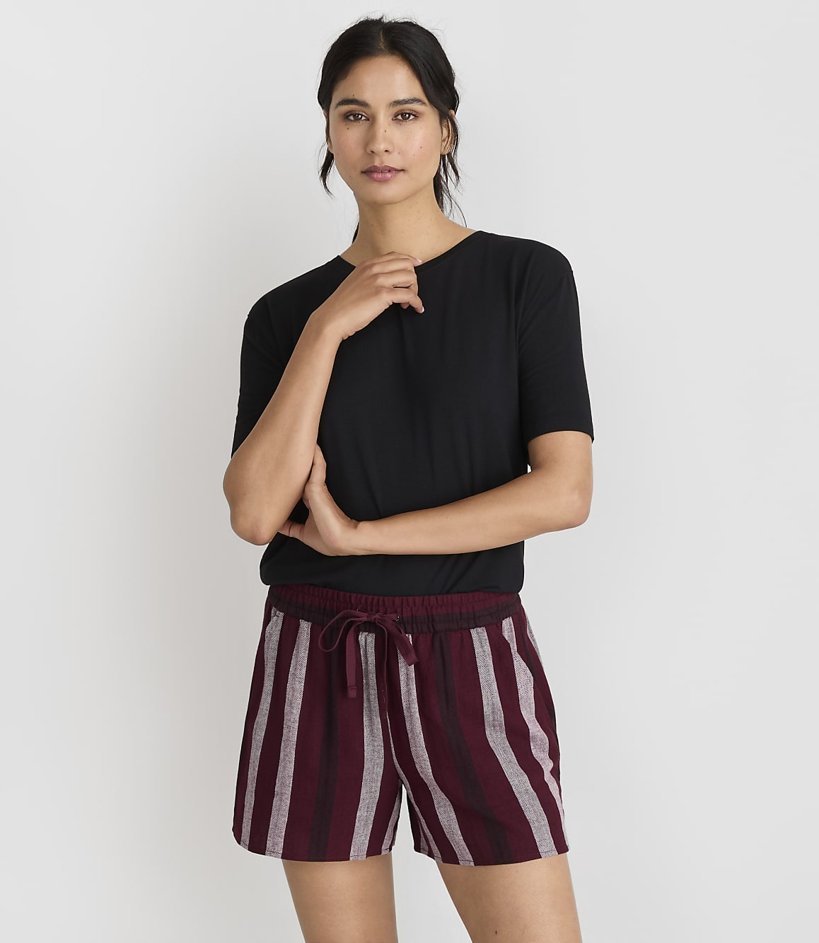 A woman in a black t-shirt and striped shorts stands against a plain white background.