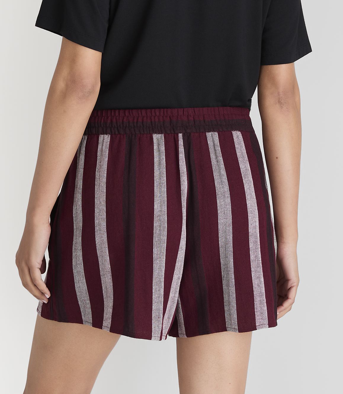 A person wearing striped burgundy and gray shorts stands against a plain gray background.