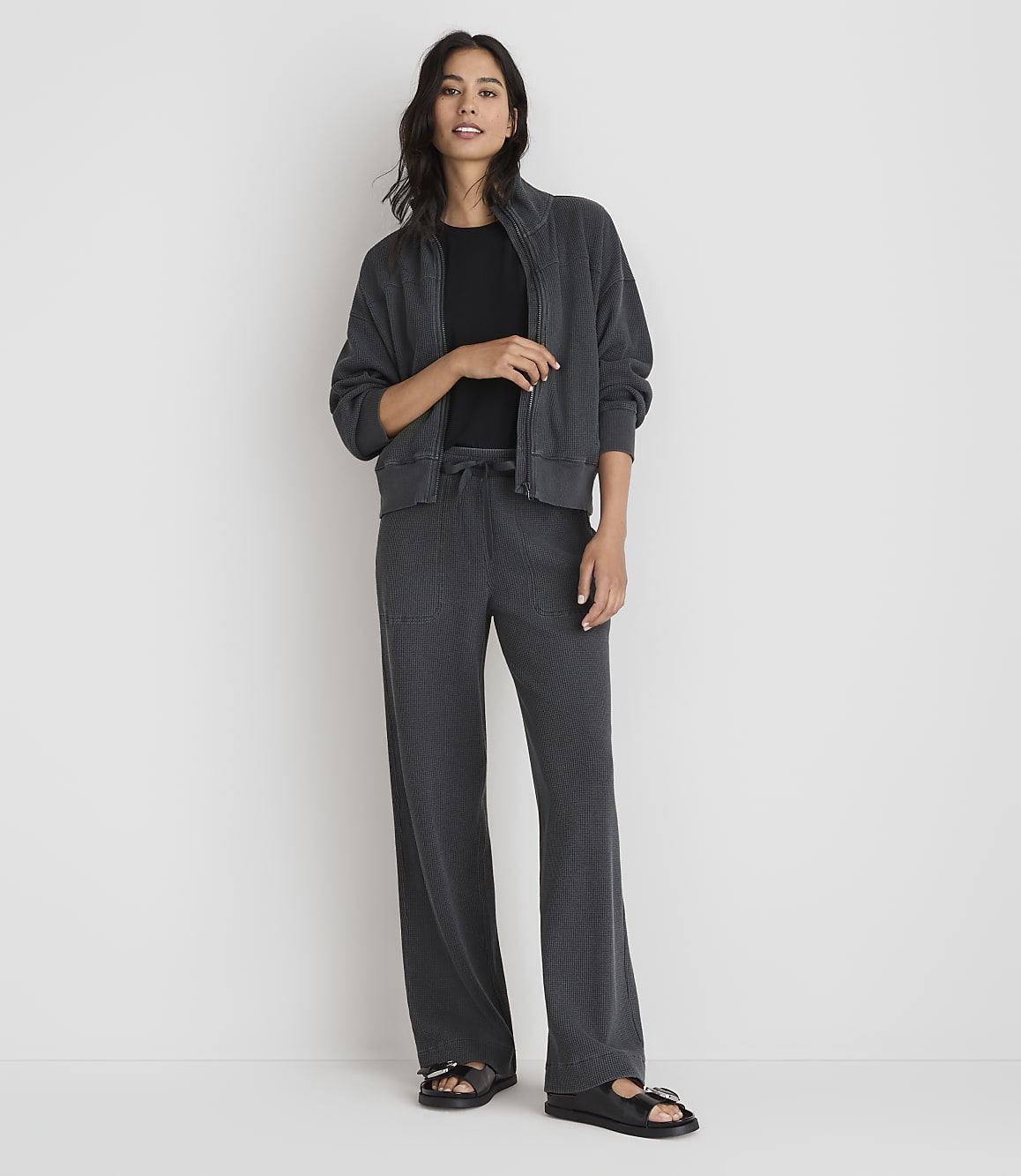 A woman in a dark grey loungewear set stands against a plain white background.