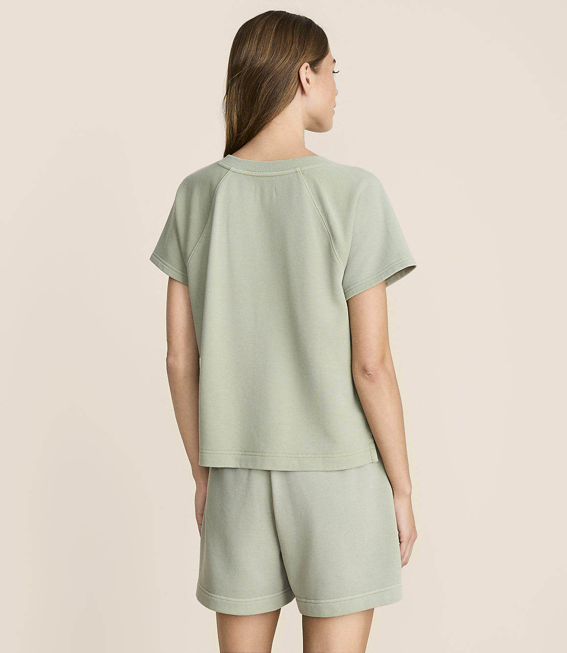 A woman in a light green t-shirt and shorts stands against a plain, light beige background.