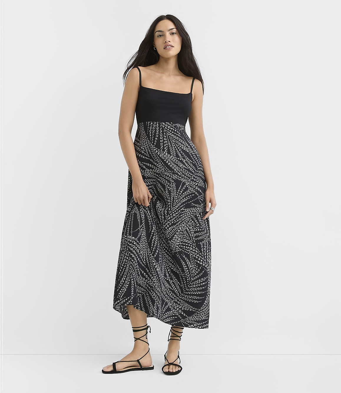 A woman in a black and white patterned maxi dress stands against a plain white background.