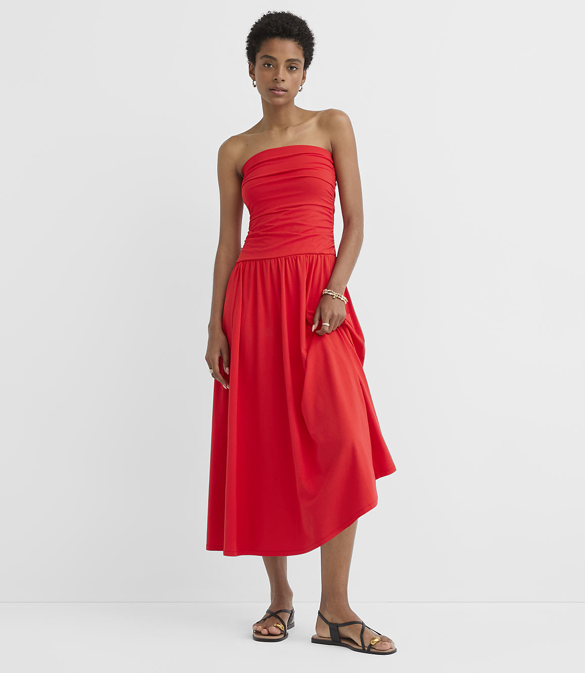 A woman in a red strapless dress stands against a plain white background.