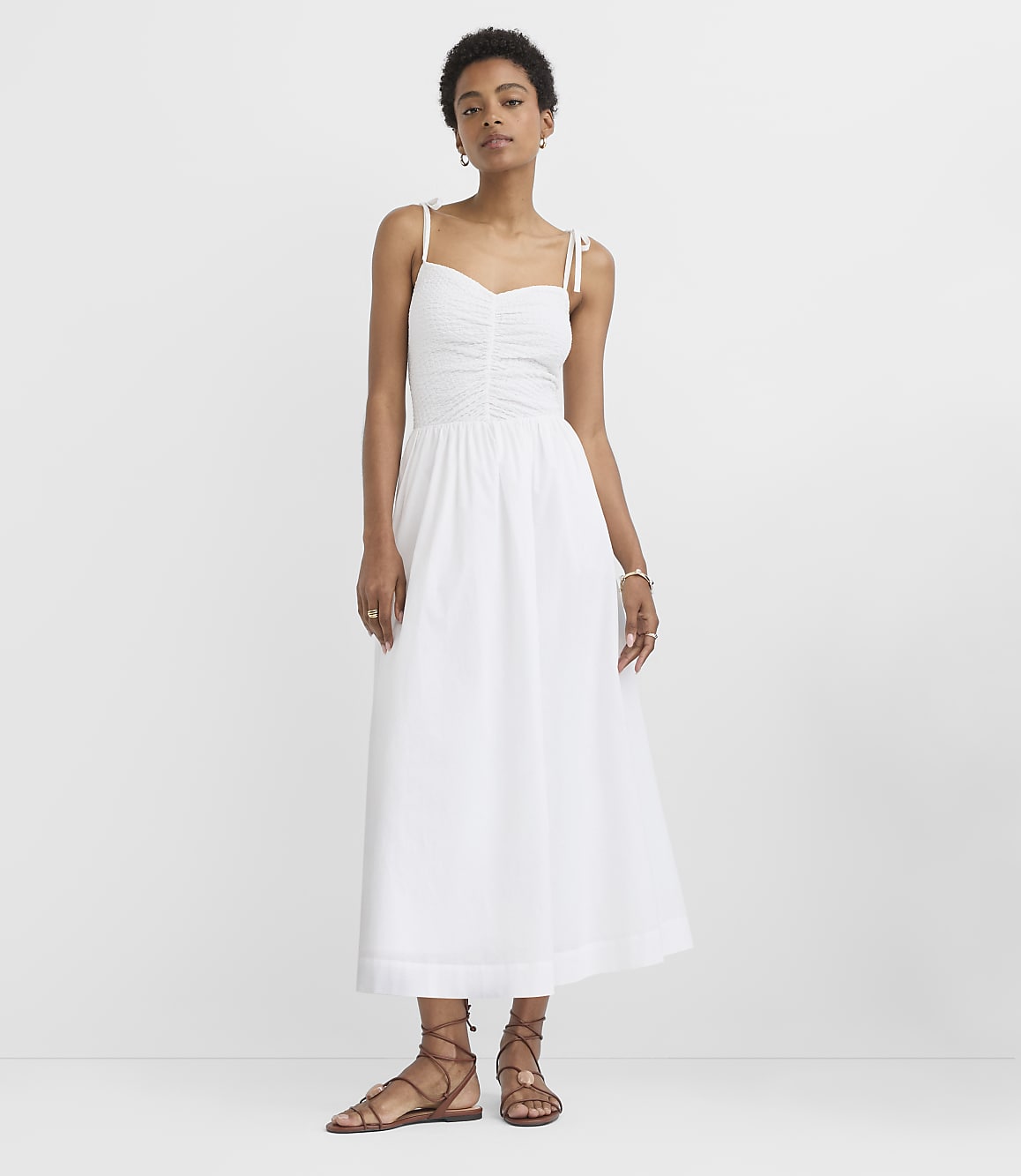 A woman in a white sundress stands against a plain white background.