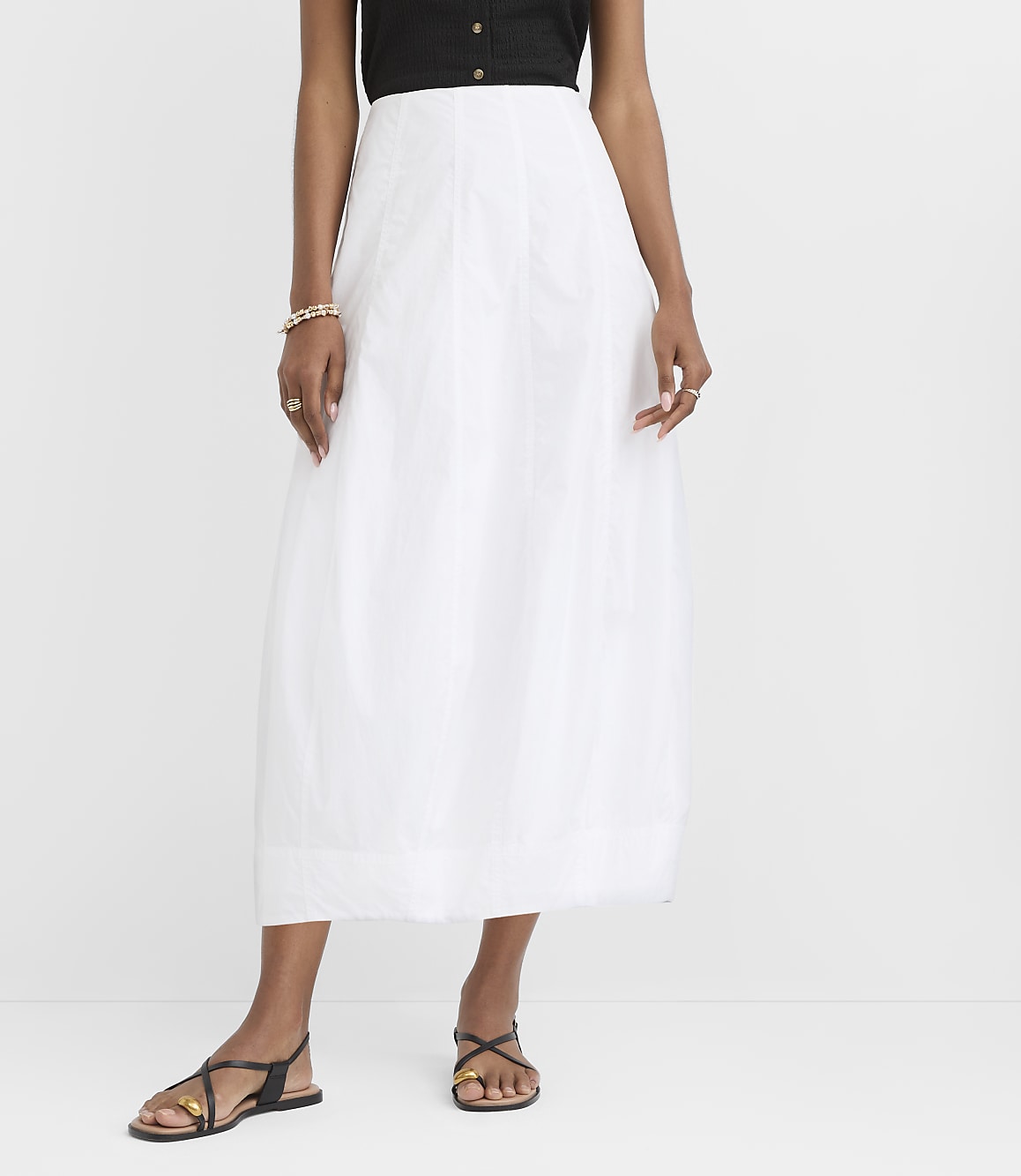 A person in a white skirt and black top stands against a plain white background.