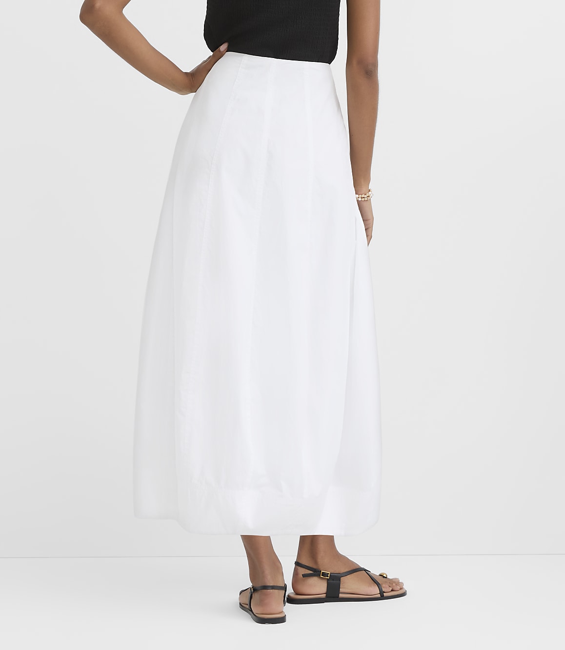 A person in a white skirt and black top stands against a plain white background.
