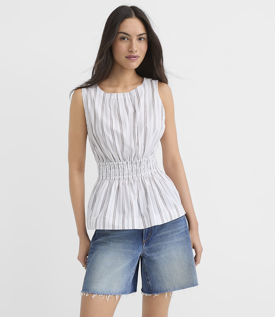 A woman in a striped peplum top and denim shorts stands against a plain white background.