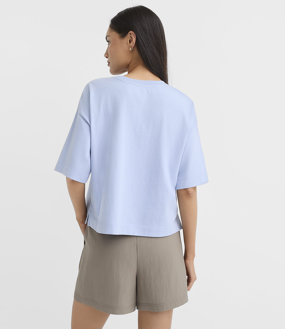 A woman in a light blue t-shirt and olive shorts stands against a plain white background.