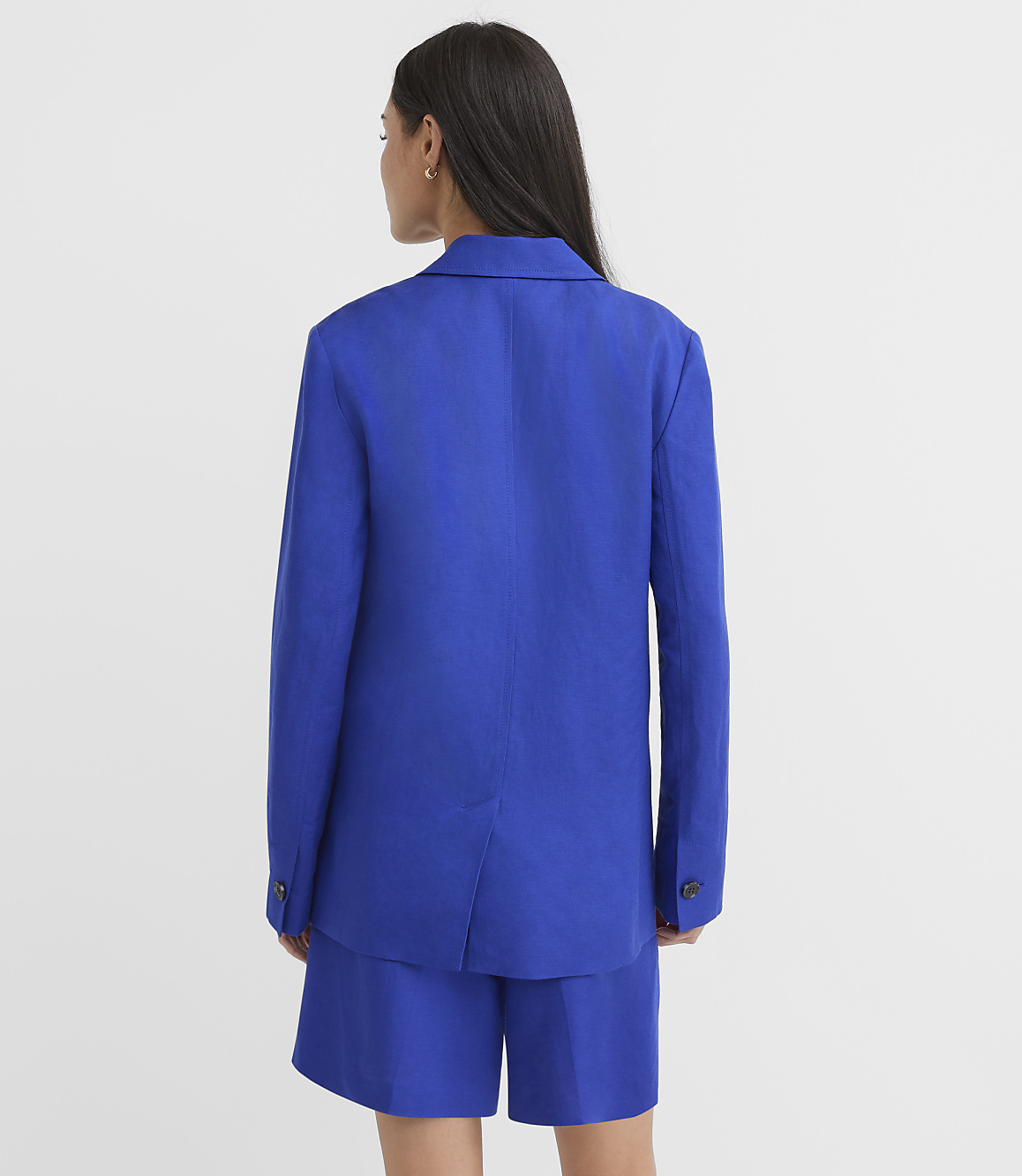 A woman in a blue blazer and shorts stands against a plain white background.