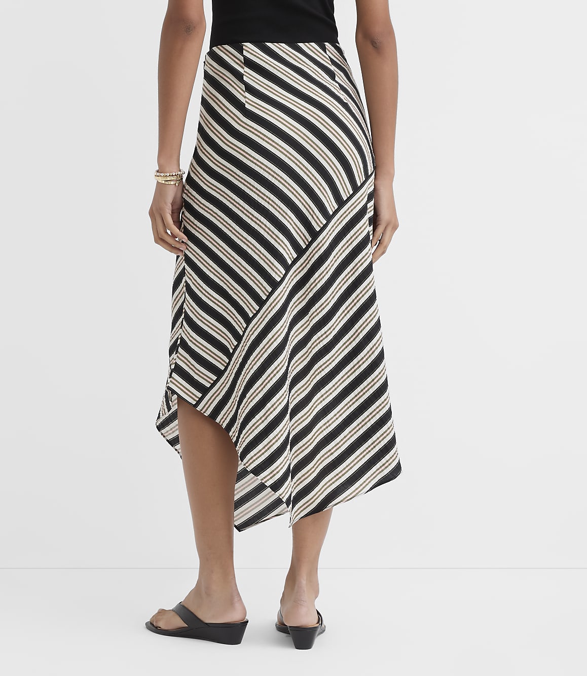 A woman in a striped asymmetrical skirt and black sandals stands against a plain white background.