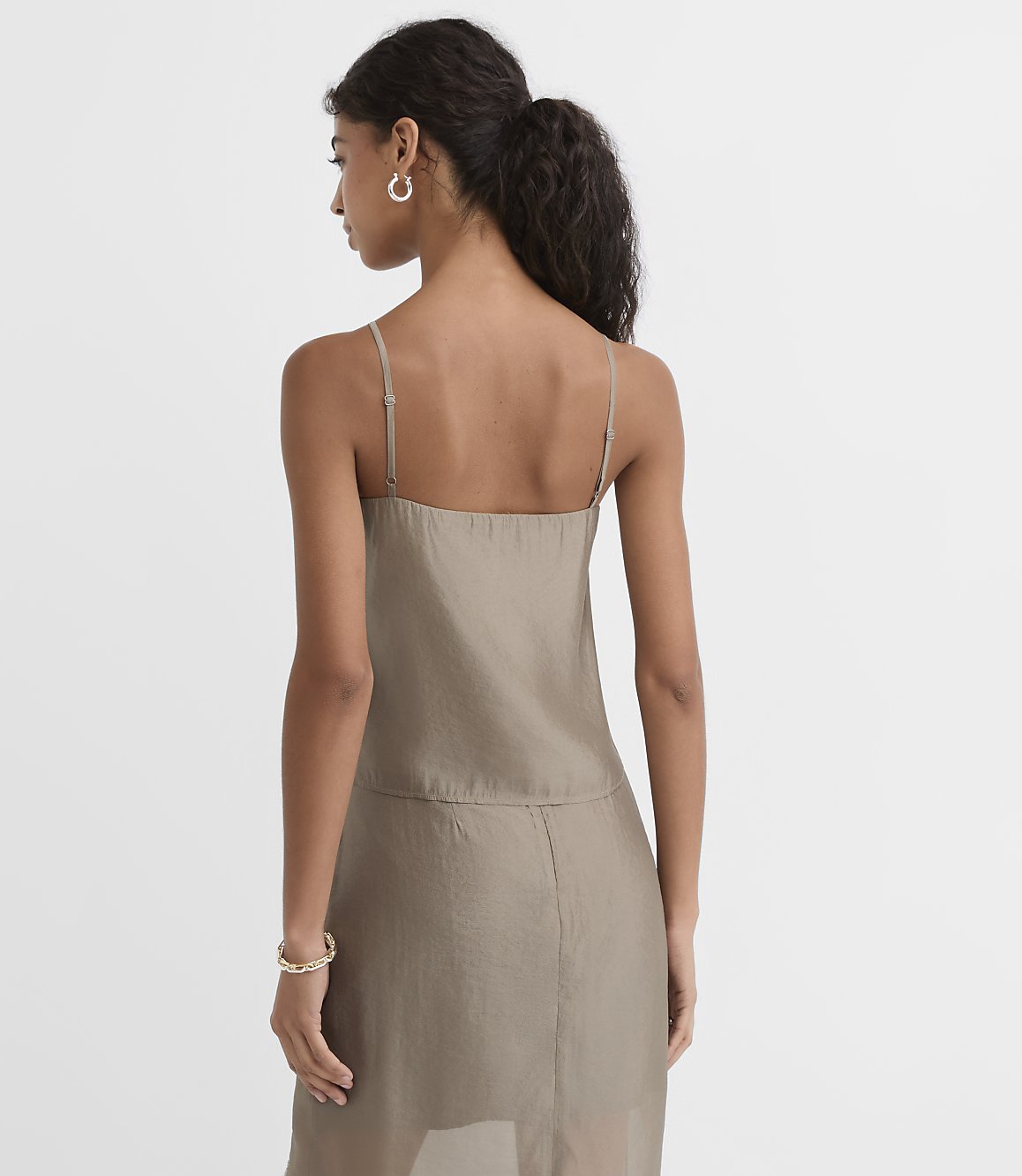 A woman in a taupe slip dress stands against a plain, light gray background.