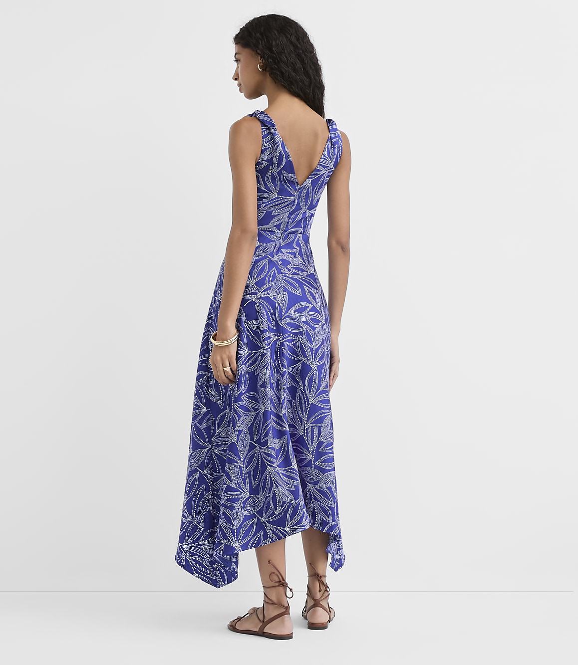A woman in a blue floral dress stands against a plain white background.