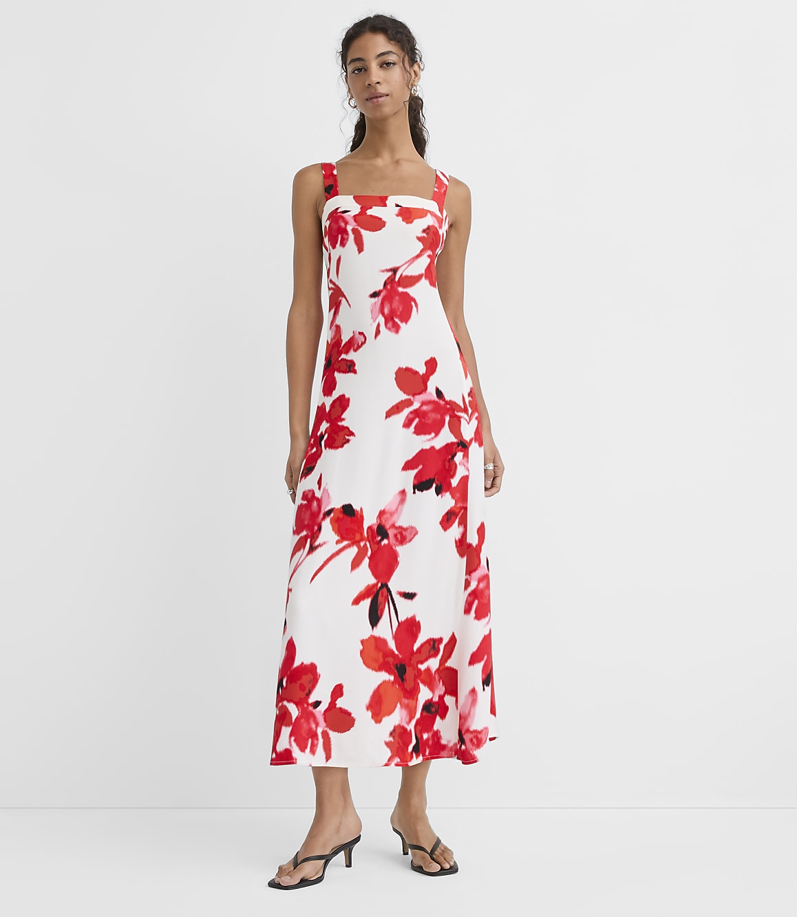 A woman in a white floral dress stands against a plain white background.