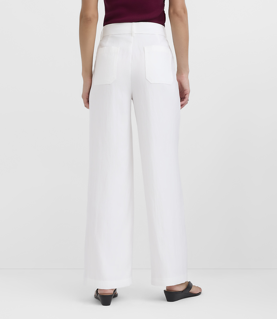 A person wearing white wide-leg pants and black sandals stands against a plain white background.