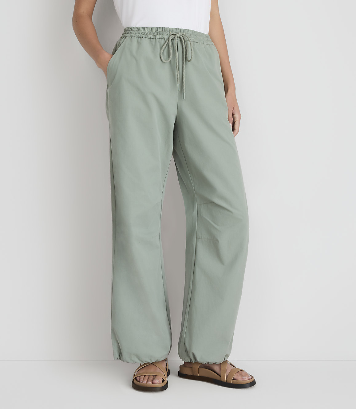 A person stands in light green pants with a drawstring waist and sandals, against a plain white background.
