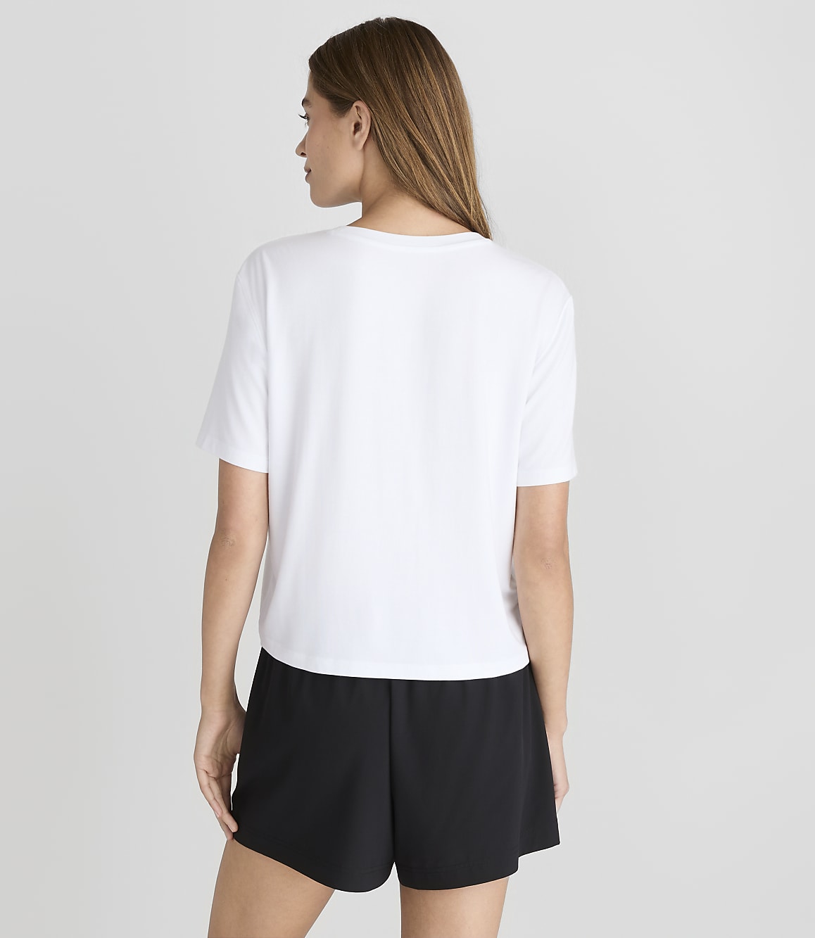A woman in a white t-shirt and black shorts stands against a plain white background.