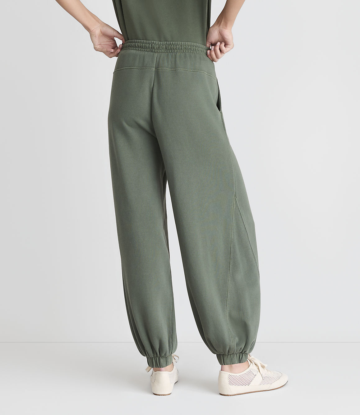 A person wearing loose-fitting green sweatpants and light-colored sneakers stands against a plain white background.