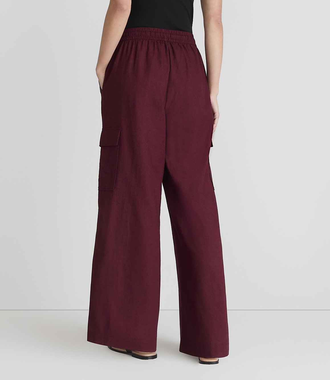 A person stands with their back to the camera, wearing maroon cargo pants and black shoes, against a plain white background.