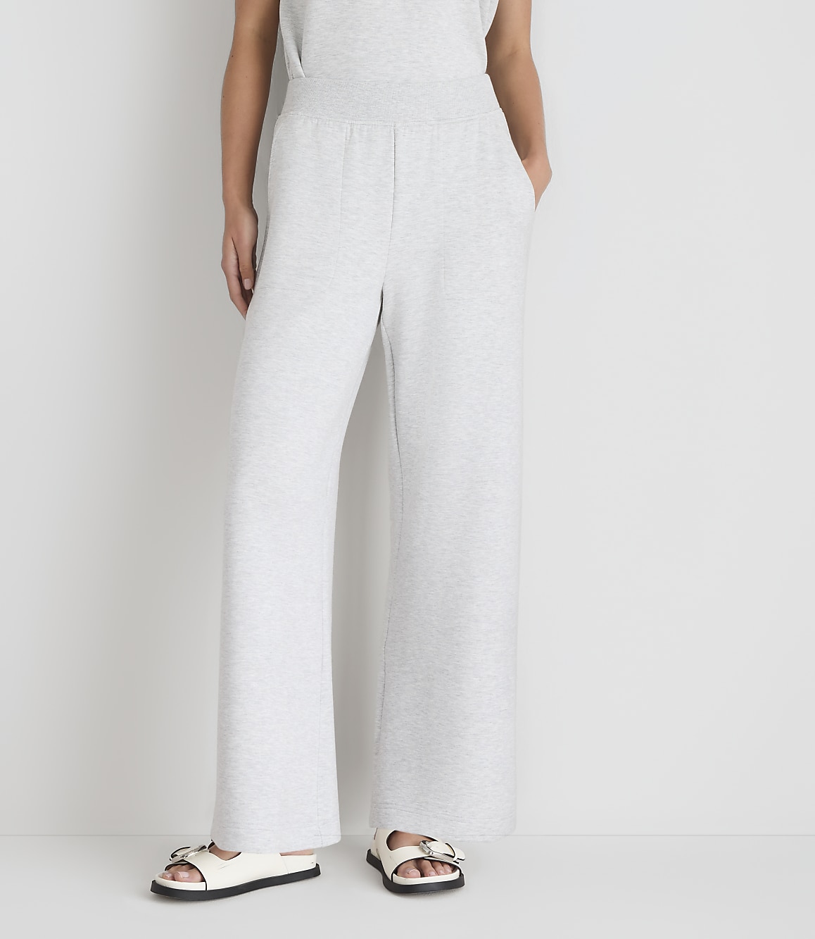 A person wearing light gray wide-leg sweatpants and white sandals stands against a plain white background.