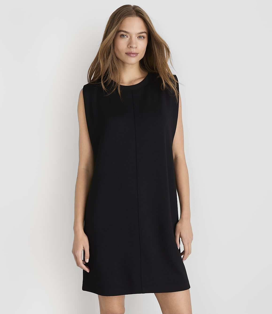 A woman in a black shift dress stands against a plain white background.