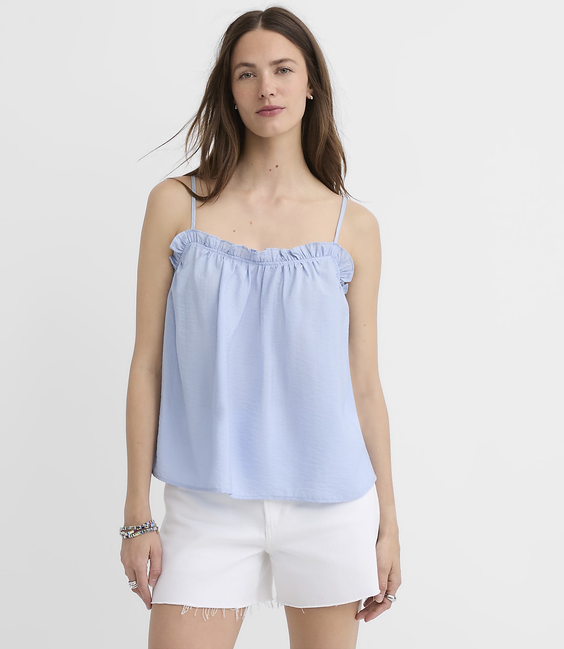 A woman in a light blue ruffled camisole and white shorts stands against a plain white background.