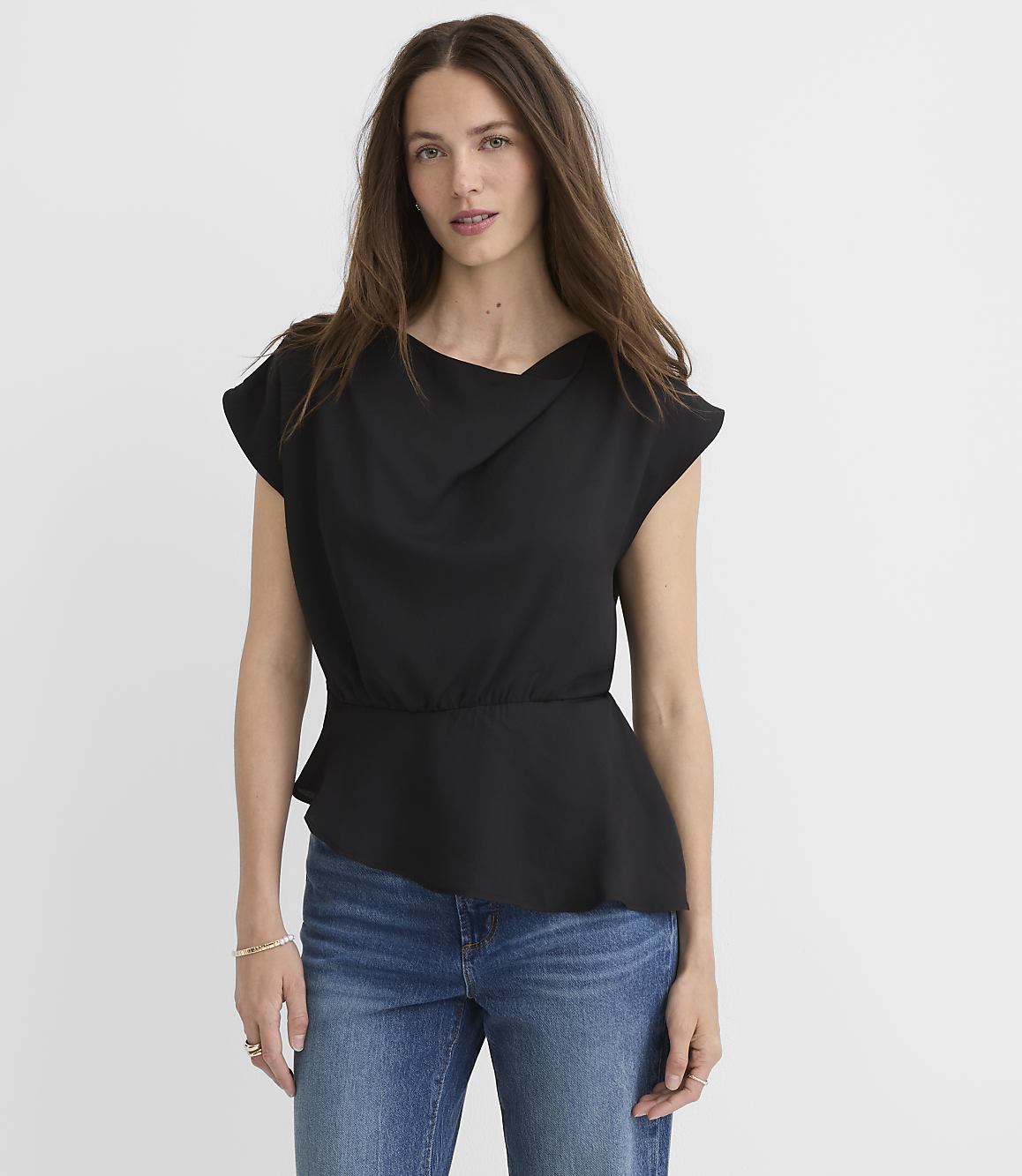 A woman in a black peplum top and blue jeans stands against a plain white background.