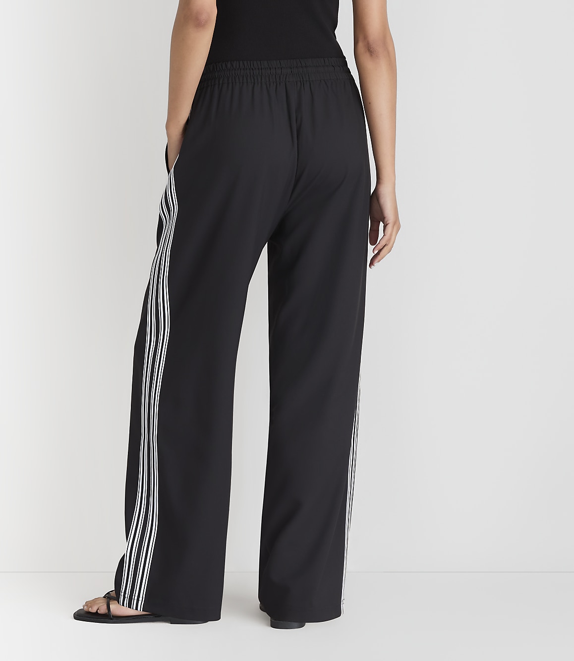 A person wearing black wide-leg pants with white stripes stands against a plain white background.