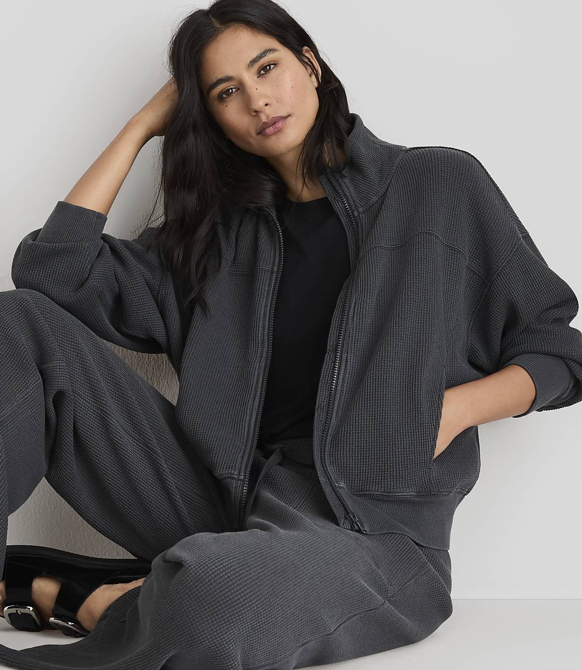 A woman in a dark grey waffle-knit jacket and pants poses against a plain white background.