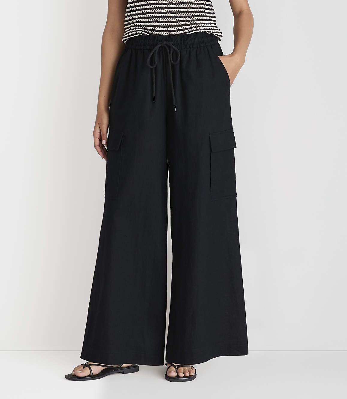 A person wearing black wide-leg cargo pants and a striped top stands against a plain white background.