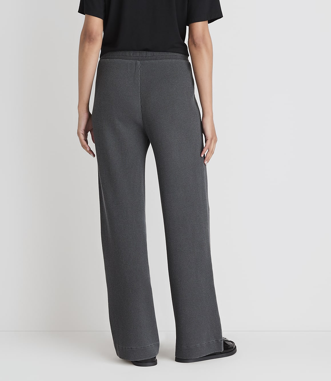 A person wearing dark gray wide-leg pants stands against a plain white background.