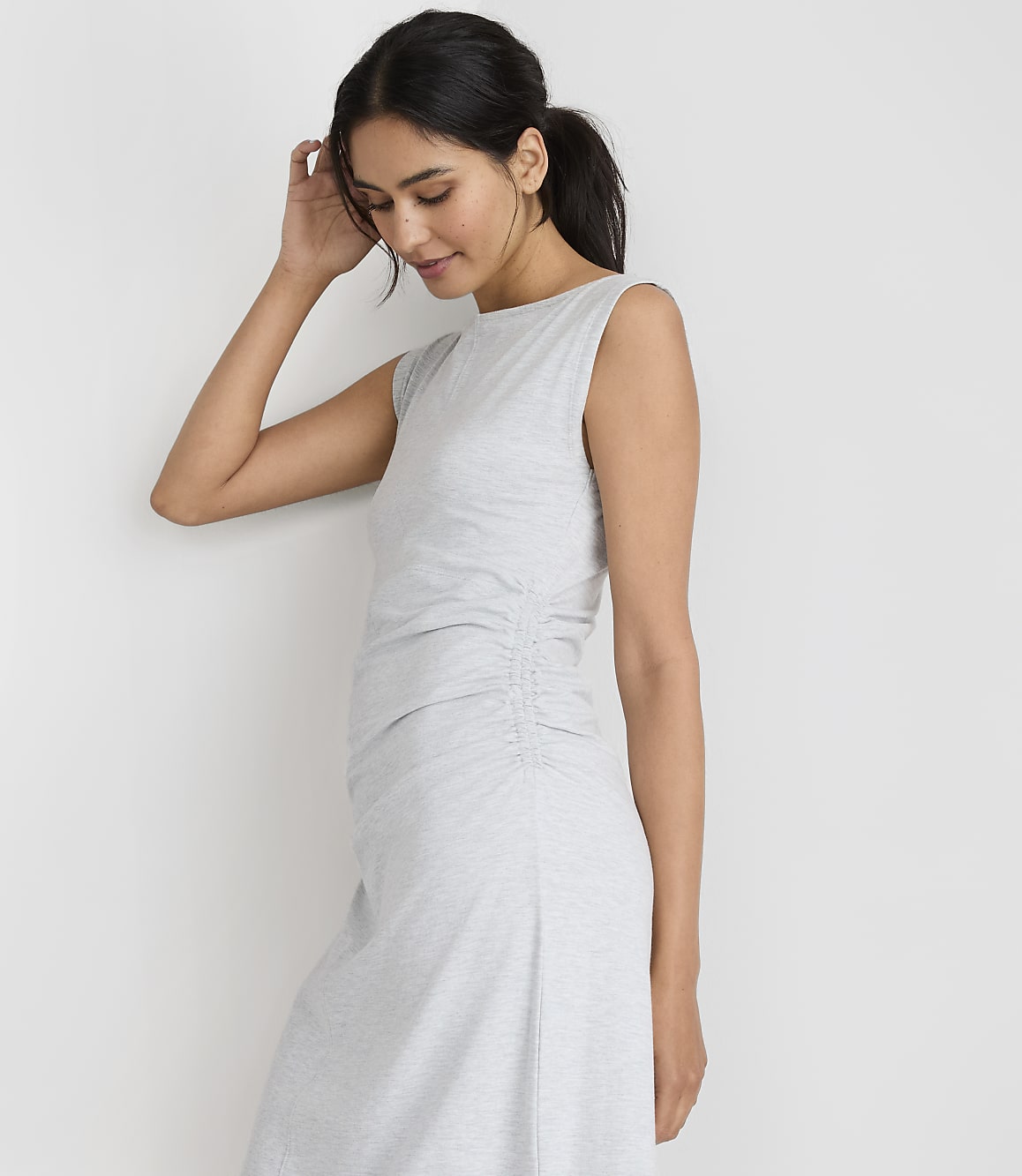 A woman in a light gray ruched dress stands against a plain white background.