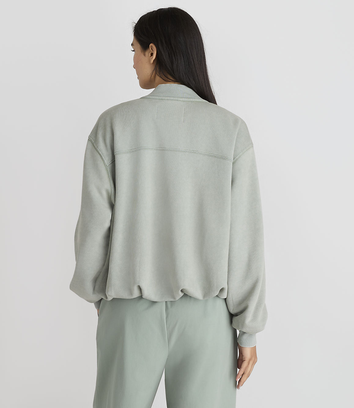 A woman in a light green sweatshirt and pants stands against a plain white background.