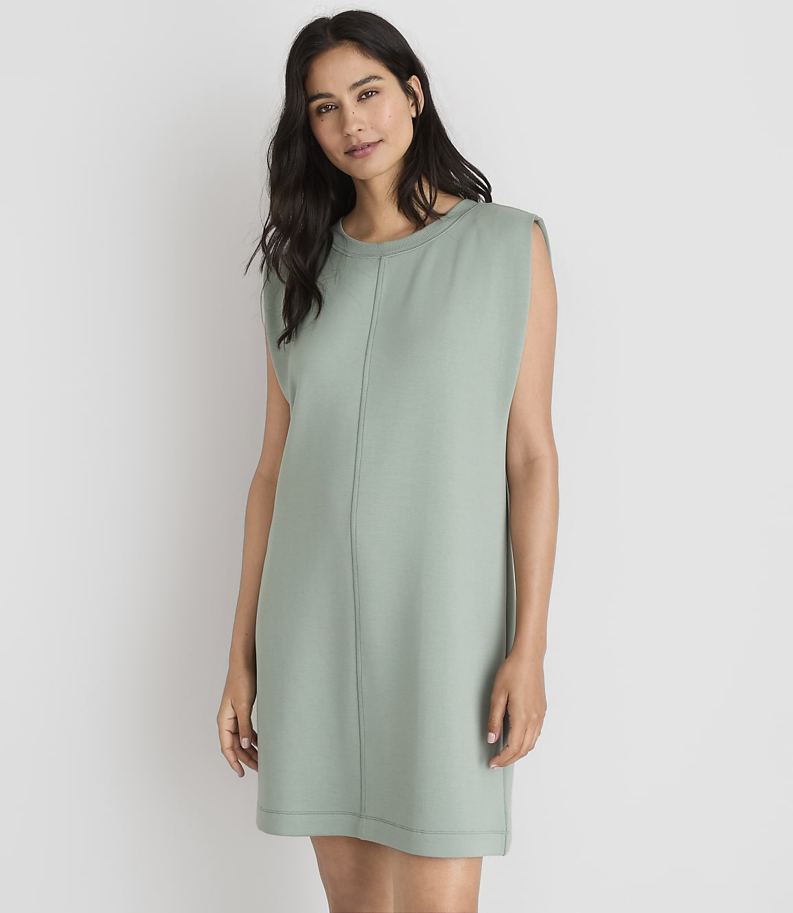 A woman in a light green dress stands against a plain white background.