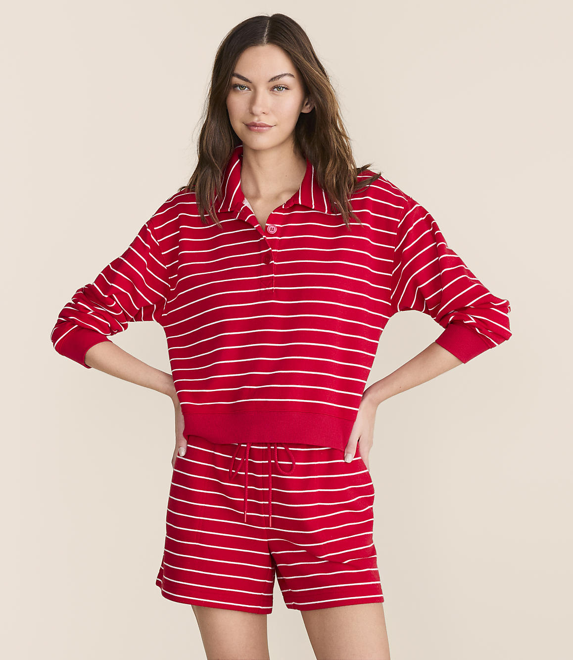 A woman in a red and white striped polo shirt and matching shorts stands against a plain, light-colored background.