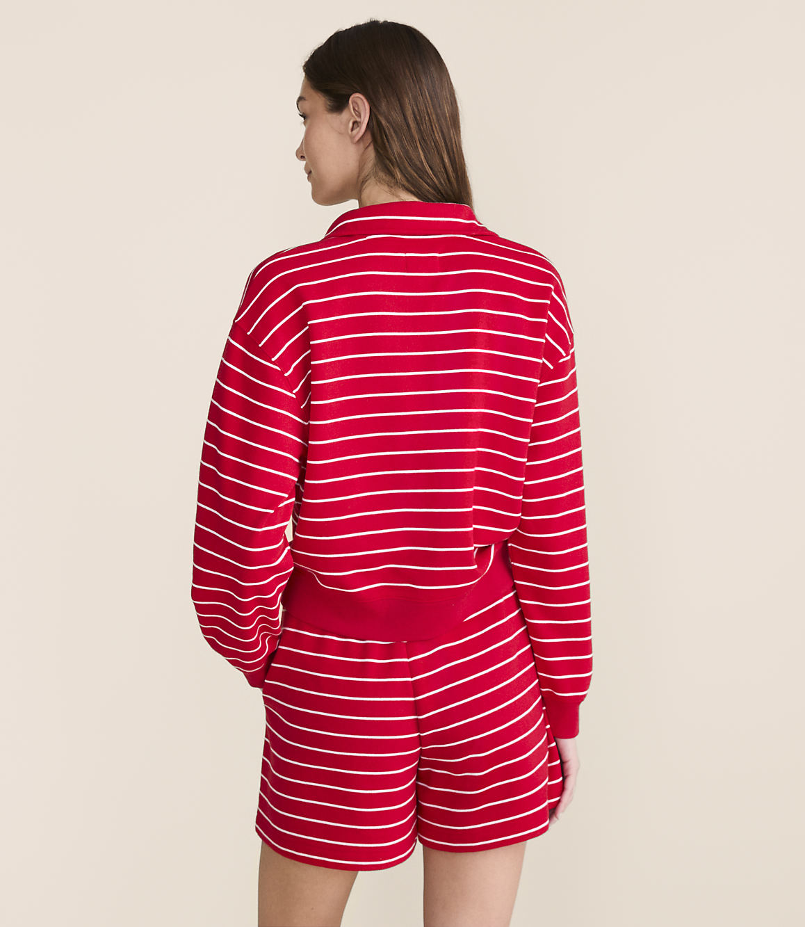A woman in a red and white striped sweatshirt and shorts stands against a plain, light-colored background.