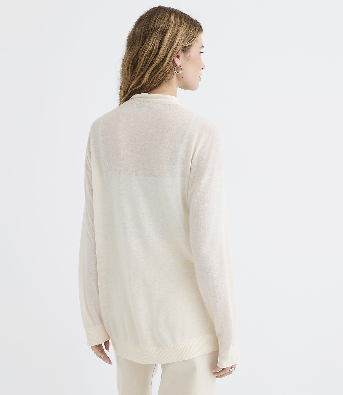 A woman in a cream-colored sweater and pants stands against a plain white background.