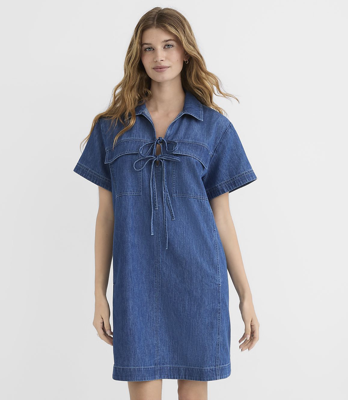 A woman in a blue denim dress stands against a plain white background.