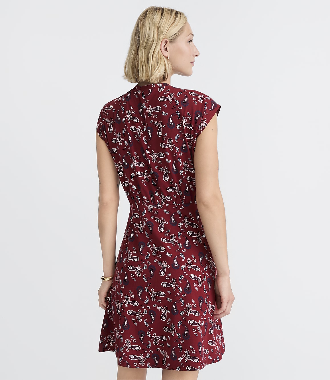 A woman in a patterned maroon dress stands against a plain white background.
