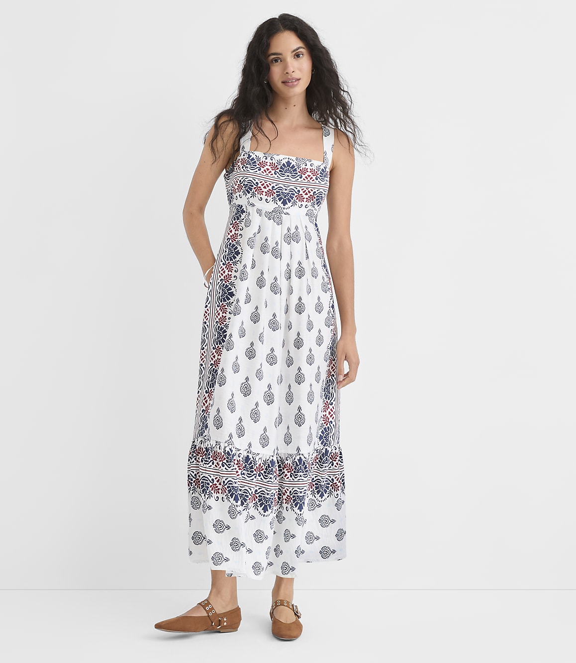 A woman in a patterned white dress stands against a plain white background.