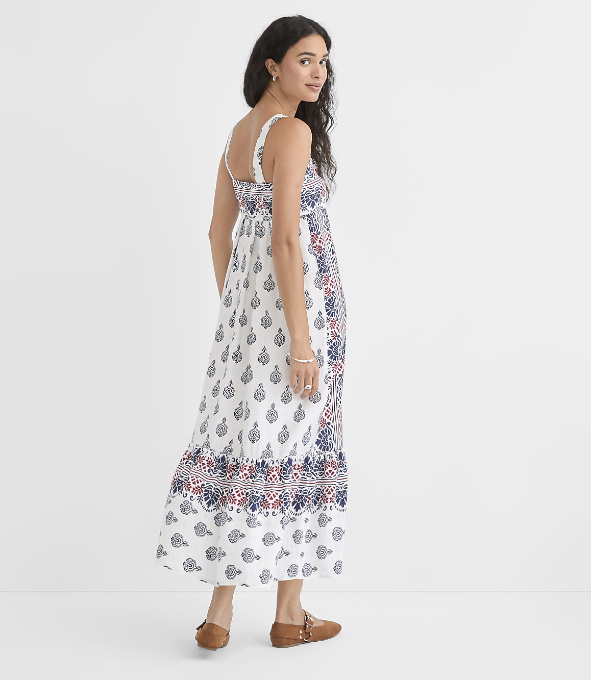 A woman in a patterned maxi dress stands against a plain white background.