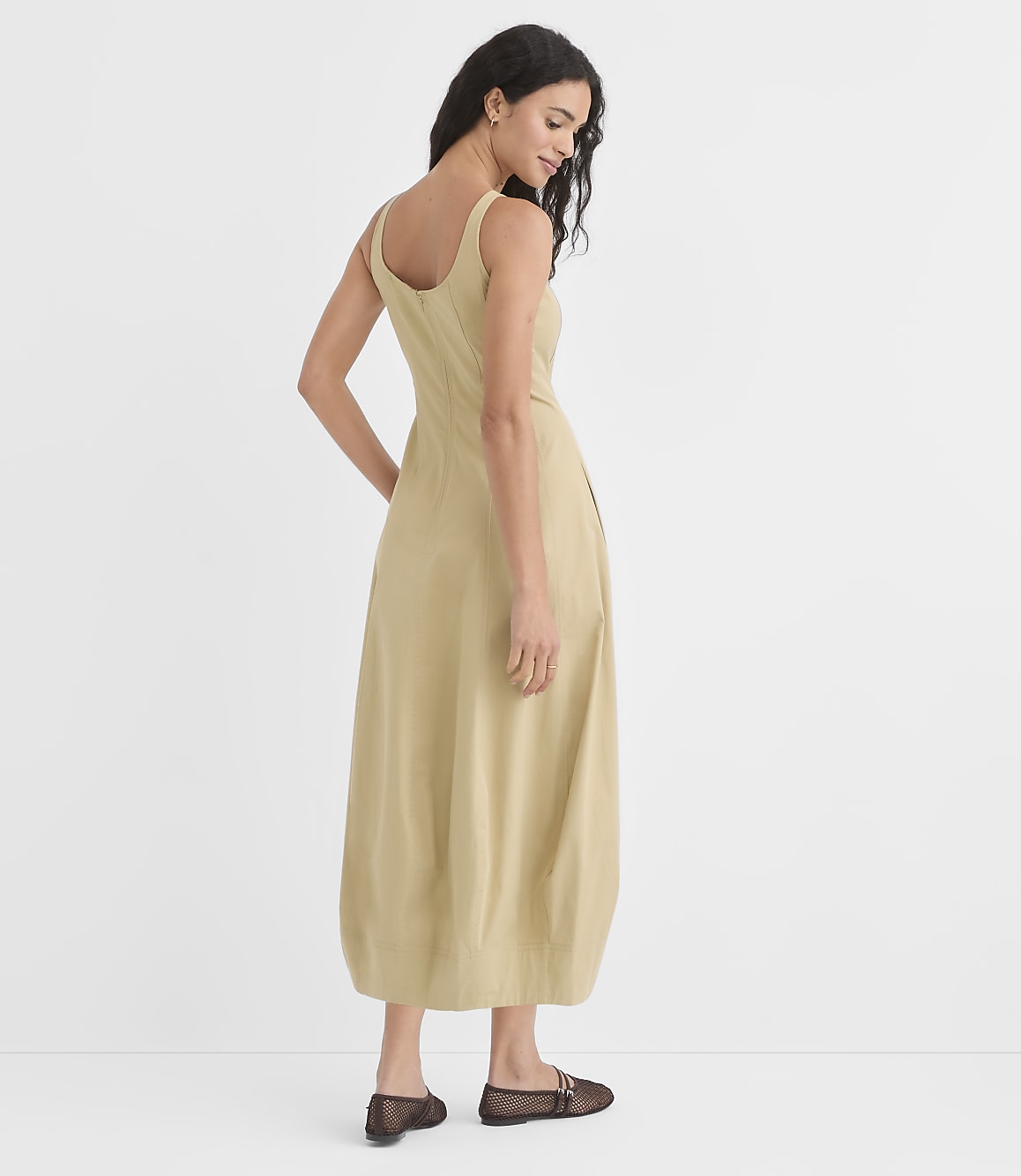 A woman in a light yellow dress stands against a plain white background.