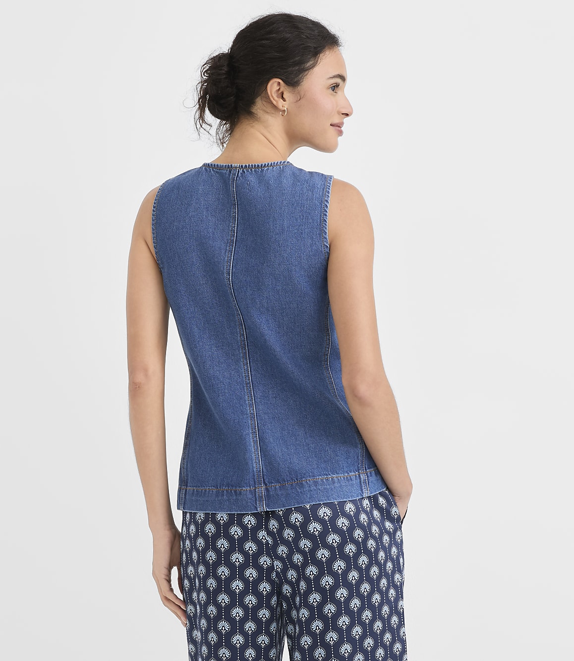 A woman in a denim top and patterned pants stands against a plain white background.