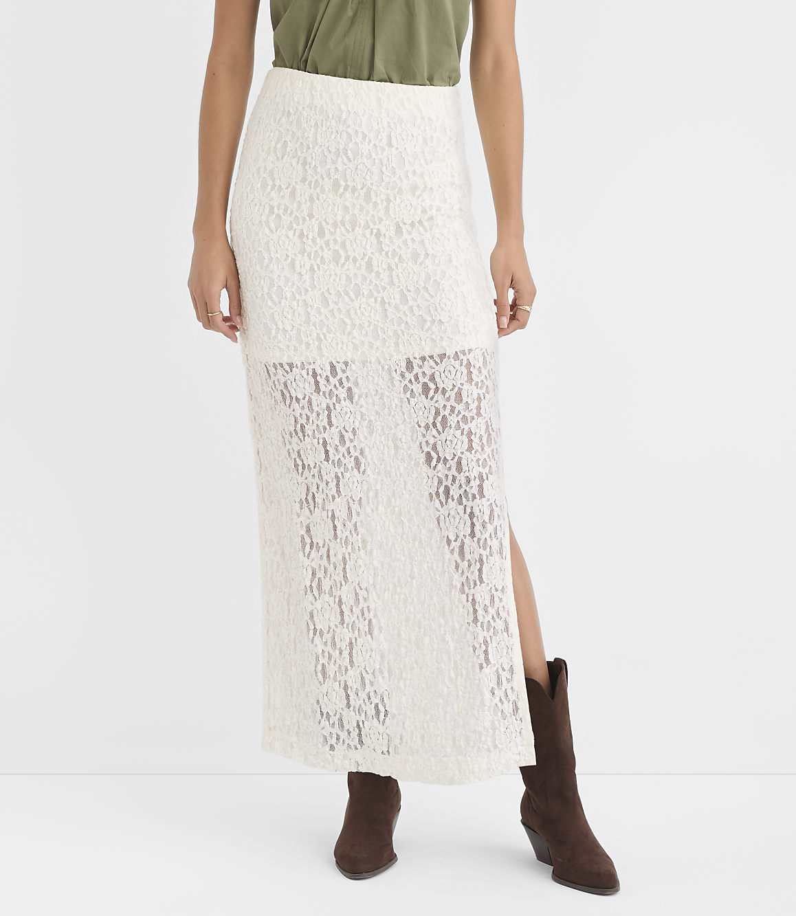 A woman in a white lace maxi skirt and brown boots stands against a plain white background.