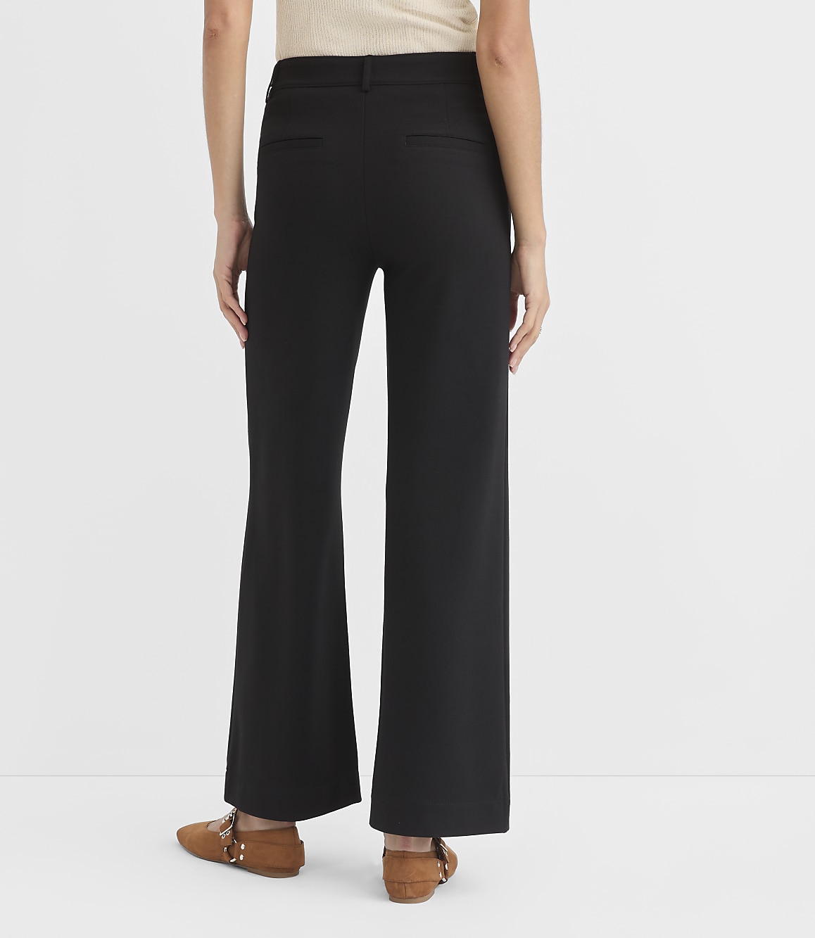 A person wearing black flared pants and brown loafers stands against a plain white background.