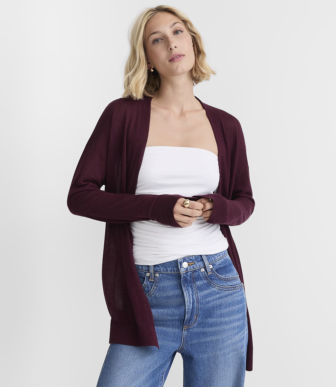 A woman in a burgundy cardigan and white tube top stands against a plain white background.