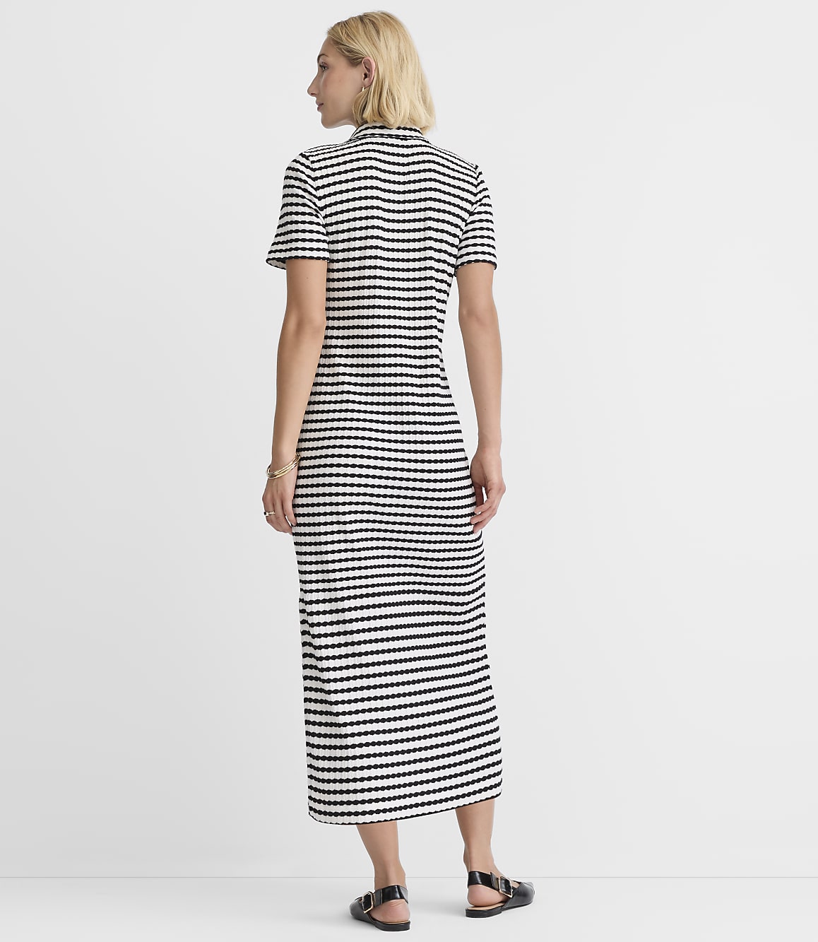 A woman in a striped dress stands against a plain white background.