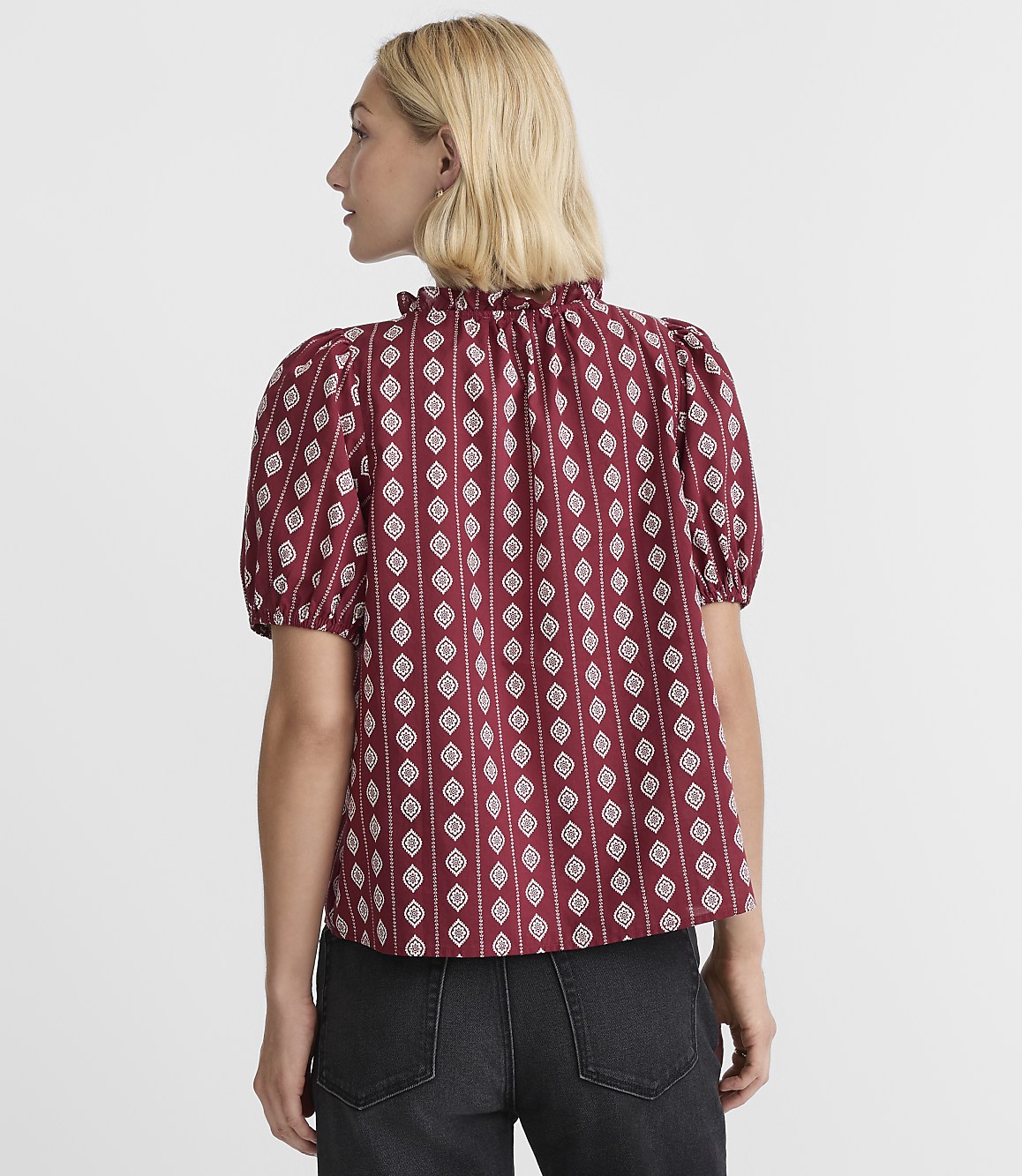 A woman in a patterned red blouse stands against a plain white background.