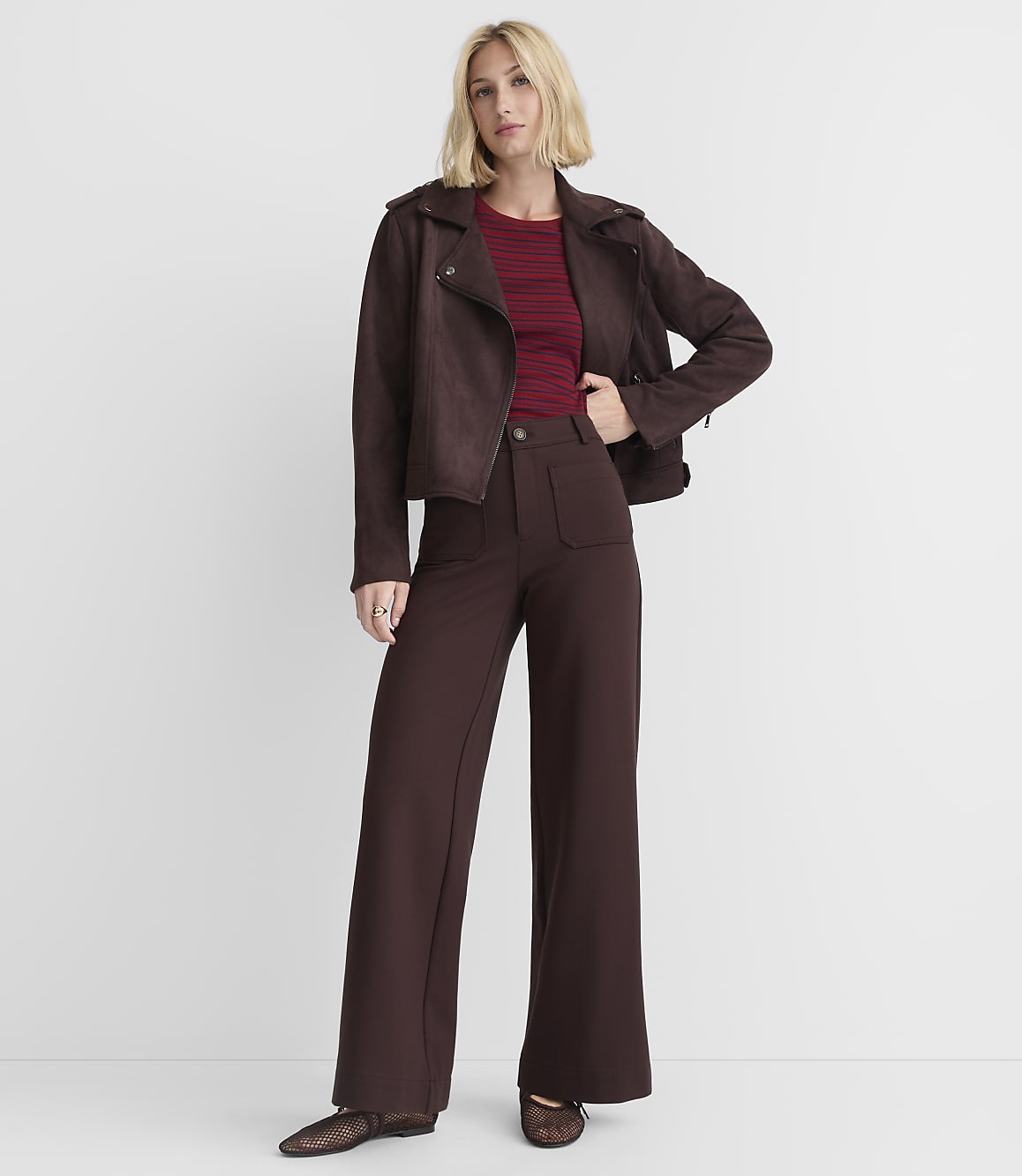 A woman in a brown jacket and pants stands against a plain white background.