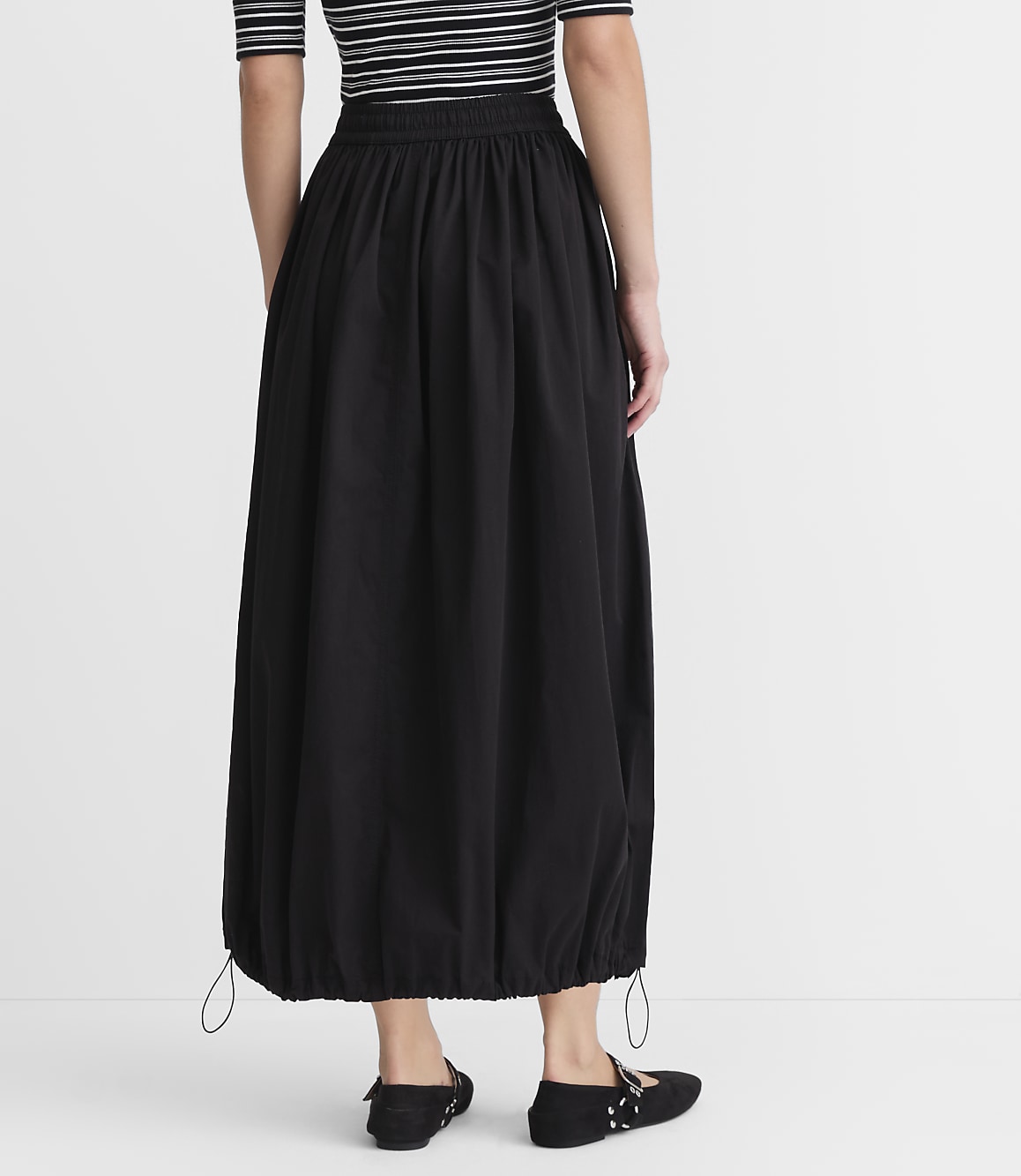 A person wearing a black balloon skirt and striped top stands against a plain white background.