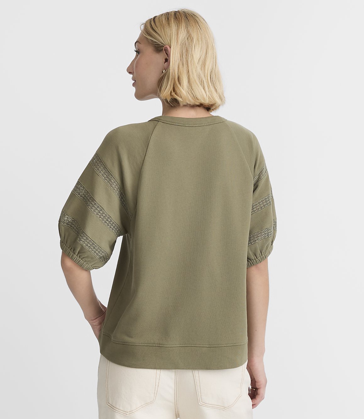 A woman in a green sweatshirt stands against a plain white background.