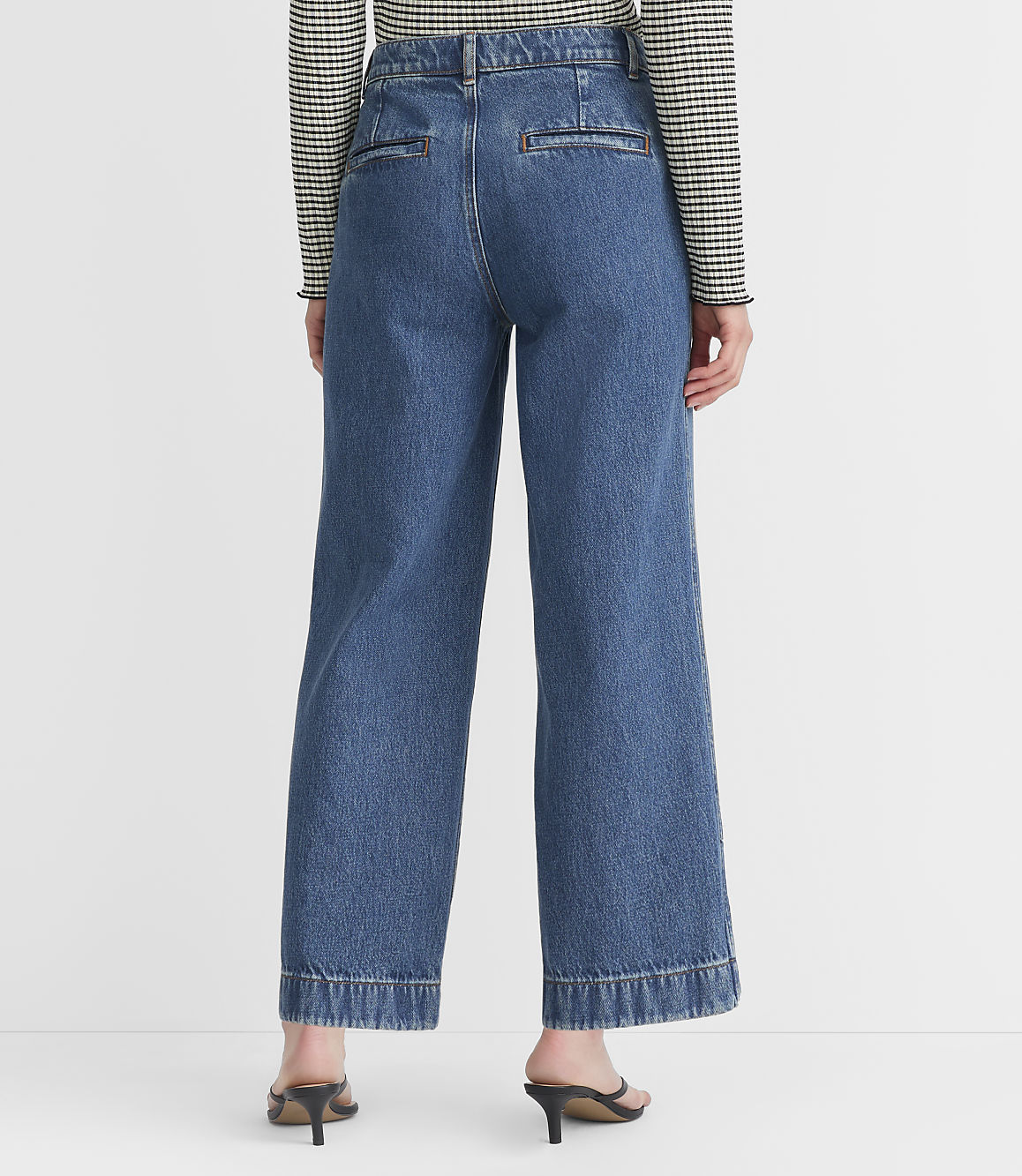 A person wearing wide-leg denim jeans and a striped shirt stands against a plain white background.